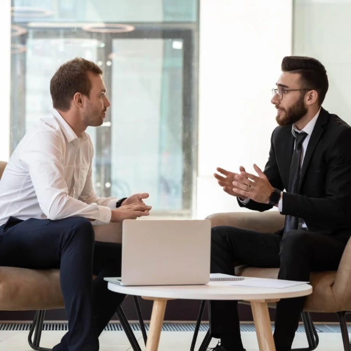 Two people discussing at a table with a laptop, representing professional services